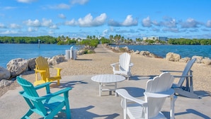 Une vue sur la plage, avec une rangée de fauteuils Adirondack et une petite table, un ciel bleu dégagé et une mer calme.