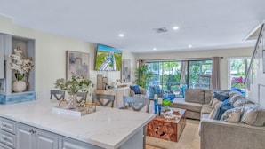 A modern kitchen with a marble countertop, dining area with chairs, a sofa, and a large window with a view of greenery. - Fall Special! 5 Star Resort Lagoon Pool Tennis GolfCart Kayaks Amenities (Key Largo)