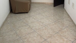 Une pièce avec un sol carrelé, un canapé recouvert d’une housse, un ventilateur de plafond et une porte.