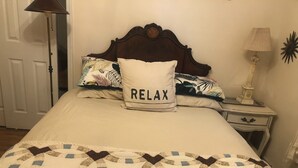 A bed with a quilt, a pillow with "RELAX" text, a nightstand, and a lamp.