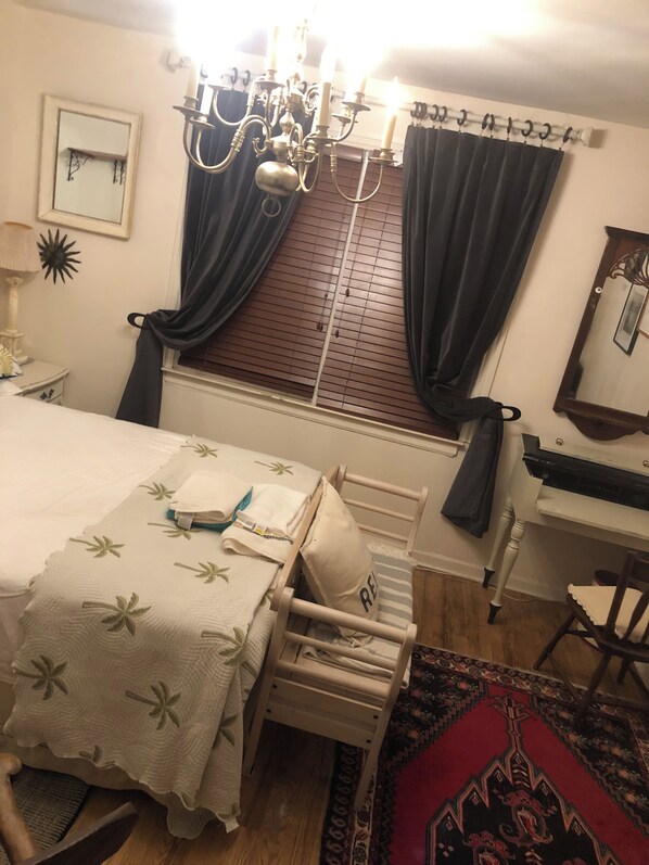 Une chambre à coucher comprenant un lit, un bureau, une chaise, une fenêtre avec des rideaux, un lustre et un miroir.
