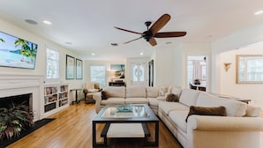 A spacious living room with a fireplace, a large sofa, a coffee table, and a ceiling fan.
