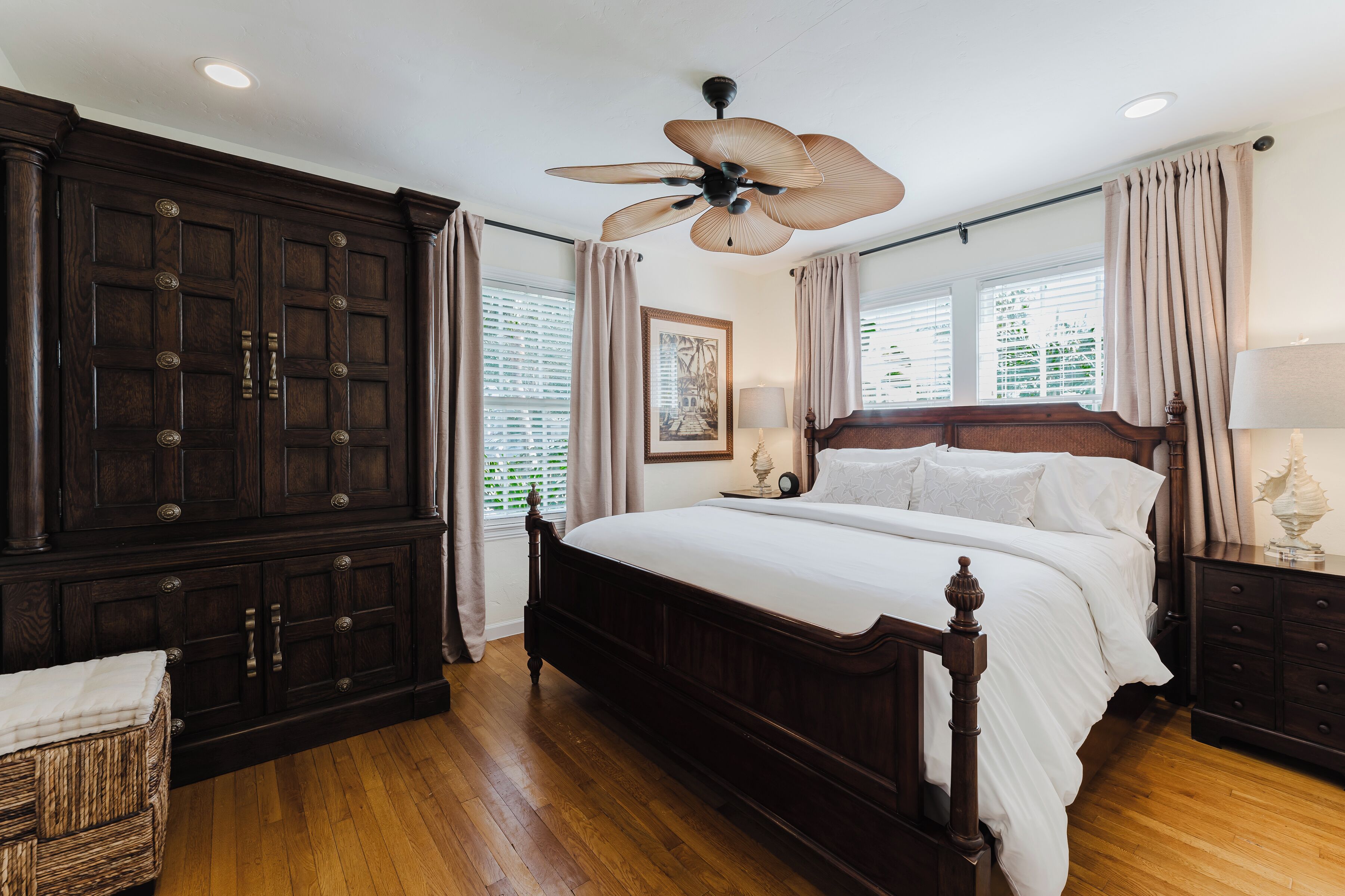 A bedroom with a large wooden bed, a ceiling fan, and a dark wooden wardrobe.
