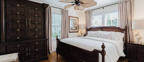 A bedroom with a large wooden bed, a ceiling fan, and a dark wooden wardrobe.