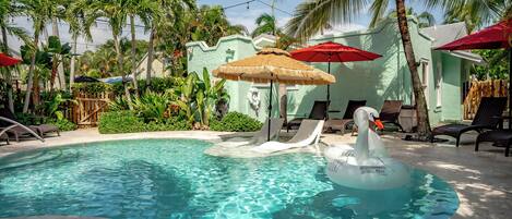 Una piscina con un flotador de cisne, sillas de descanso y palmeras.