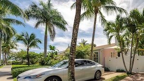 A white car parked on a brick driveway with palm trees and a house in the background. - Coco Plum Cottage (West Palm Beach)