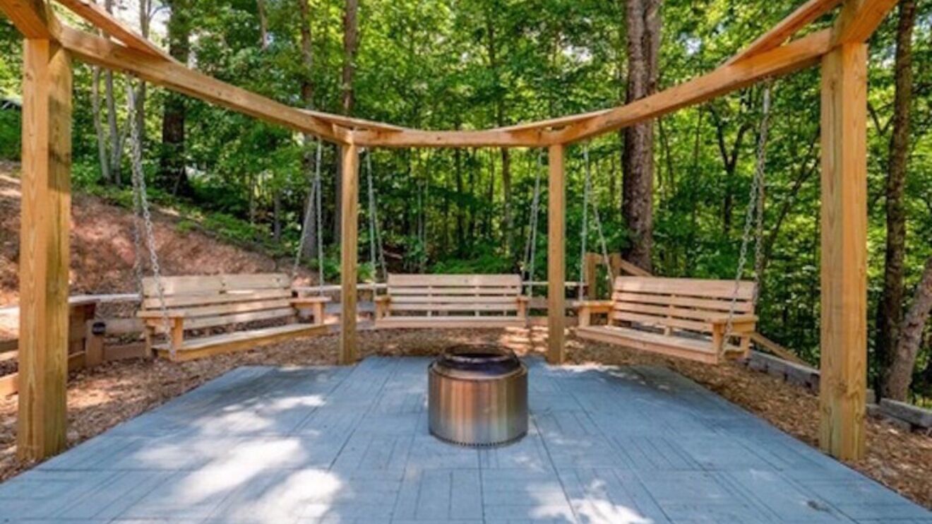 A wooden gazebo with benches and a fire pit in a forested area.