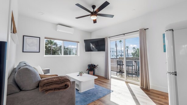 Un salon moderne doté d’un ventilateur de plafond, d’un téléviseur à écran plat, d’un canapé, d’une table basse et d’un balcon avec des meubles d’extérieur.