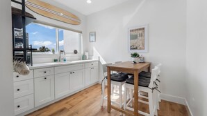 Une cuisine moderne avec des meubles blancs, une table en bois et une fenêtre donnant sur un ciel bleu.