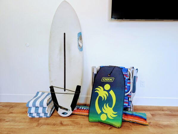 A surfboard, a towel, and a bag with a surfboard design on a wooden floor. - Rise Suites Oceanside (Oceanside)