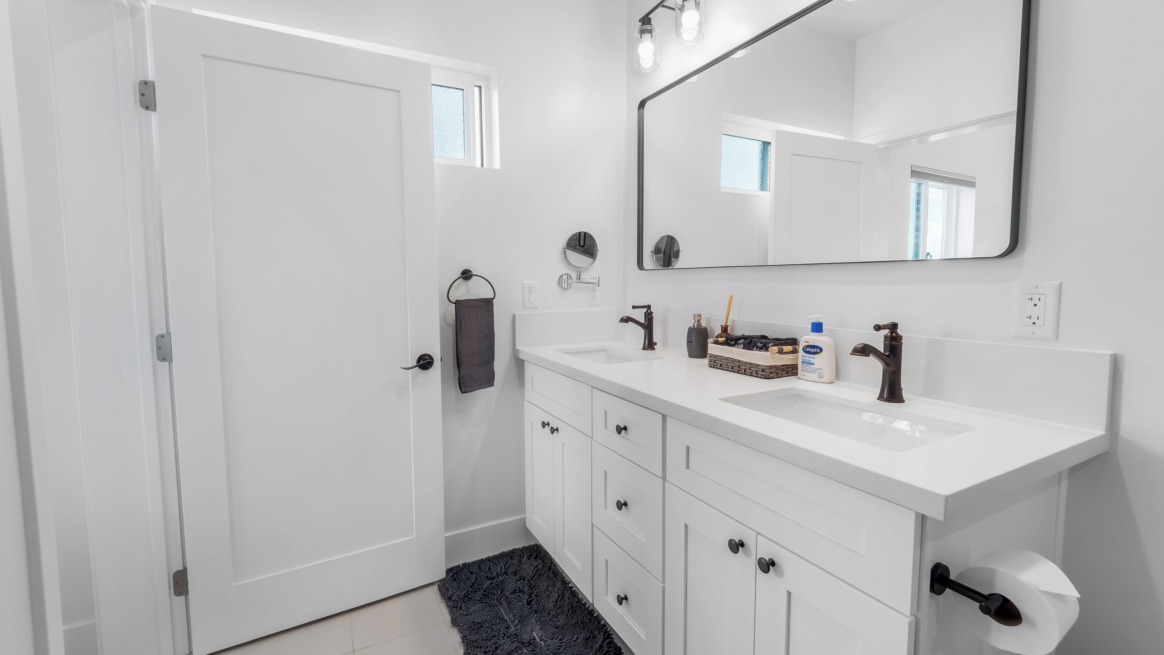 A modern bathroom with a white vanity, a large mirror, a towel rack, and a toilet paper holder.