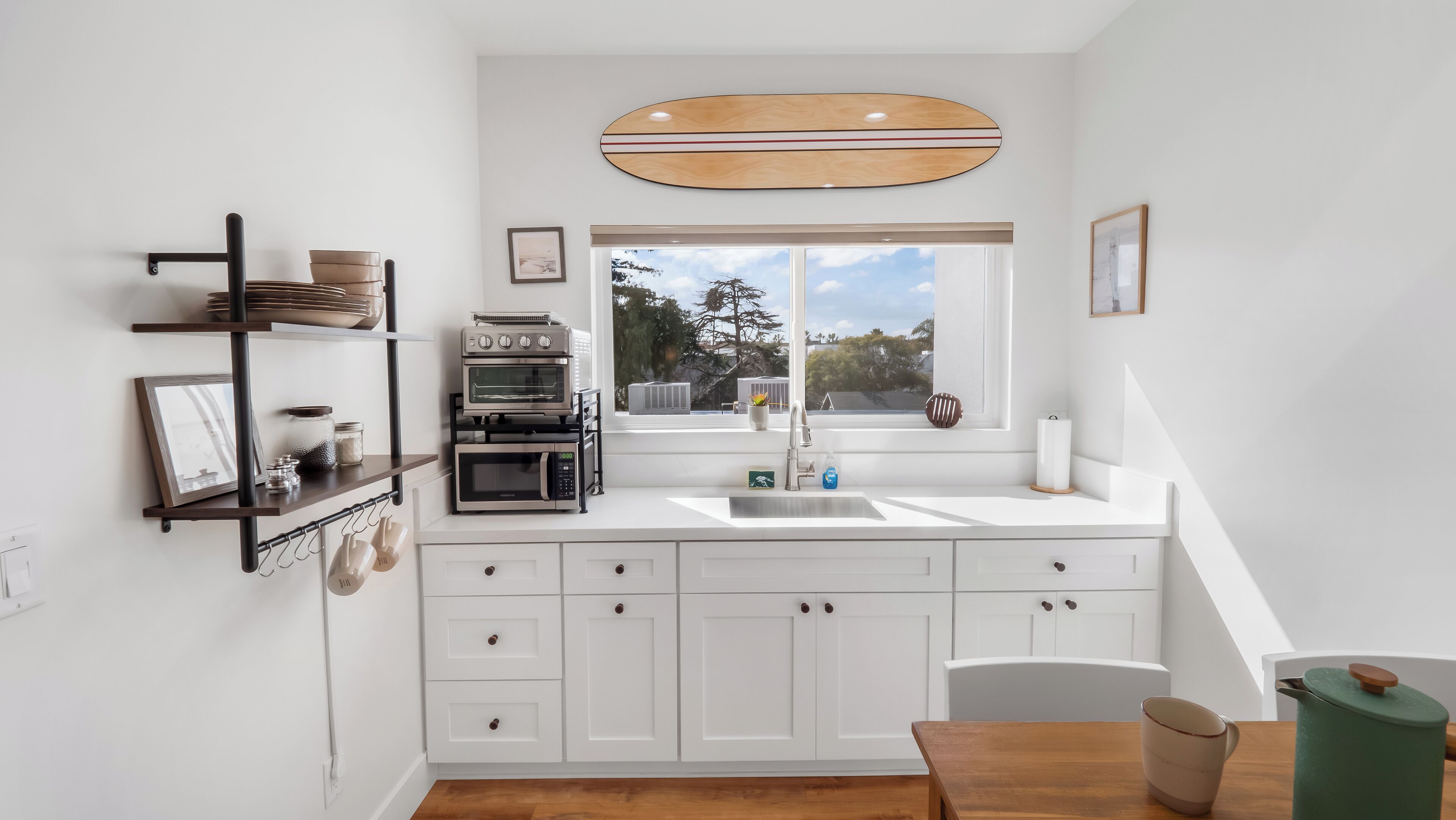 Una cucina moderna con mobili bianchi, forno integrato, microonde e un'ampia finestra che offre vista su alberi e un cielo sereno.