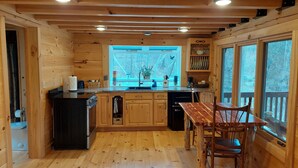 A wooden cabin kitchen with a central island, wooden cabinets, and a dining area with a table and chairs. - Tranquil Amish-built cabin near Wildcat State Park (Ontario)