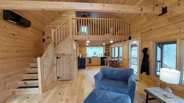 A wooden cabin interior with a staircase leading to a loft bedroom, a dining area, and a kitchen. - Tranquil Amish-built cabin near Wildcat State Park (Ontario)