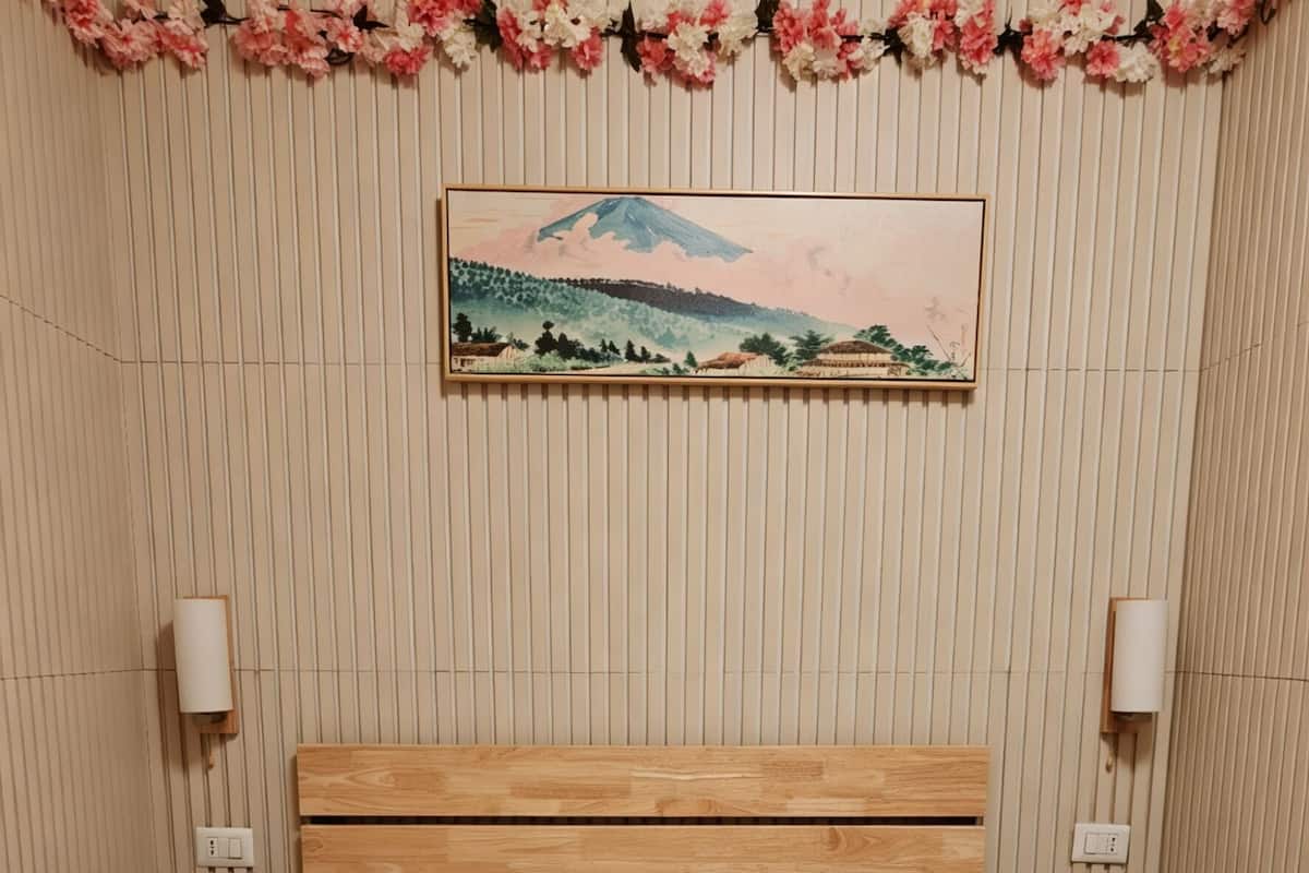 A hotel room with a bed, a wall-mounted painting, and a floral garland.