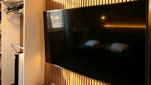 A modern living room with a flat-screen TV, a wooden slat wall, a clock, and a small white cabinet with a vase of flowers. - BED & BREAKFAST SAKURA (Milan)