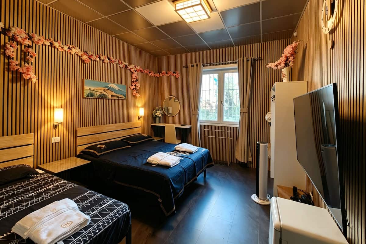 A hotel room with two beds, a desk, a TV, and a window with curtains.