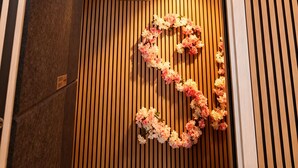 A hotel entrance with a wooden slat wall, a floral decoration, and an air conditioning unit above. - BED & BREAKFAST SAKURA (Milan)