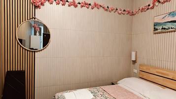 A bedroom with a bed, a round mirror, a wooden chair, and a wall-mounted light fixture.