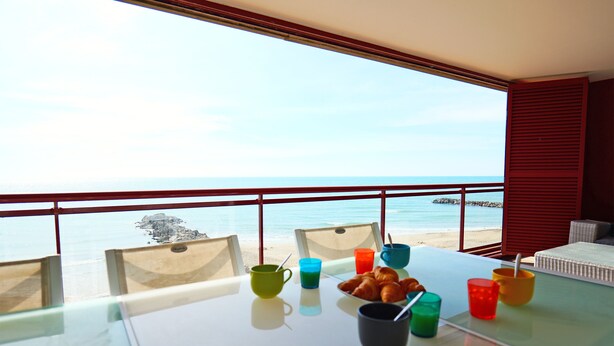 Un balcón con una mesa dispuesta para el desayuno, con vista a una playa.