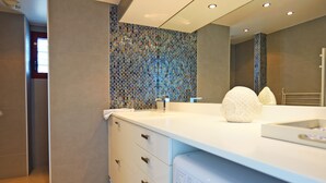 Un baño moderno con encimera blanca, un espejo grande y pared de azulejos.