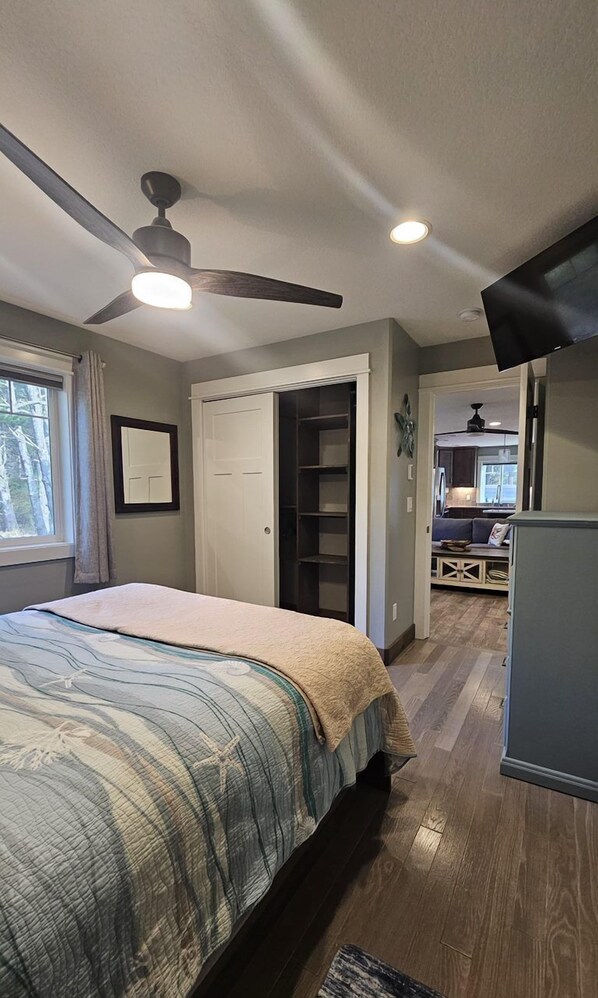 Une chambre à coucher comprenant un lit, un ventilateur de plafond, un dressing et donnant sur un coin cuisine.