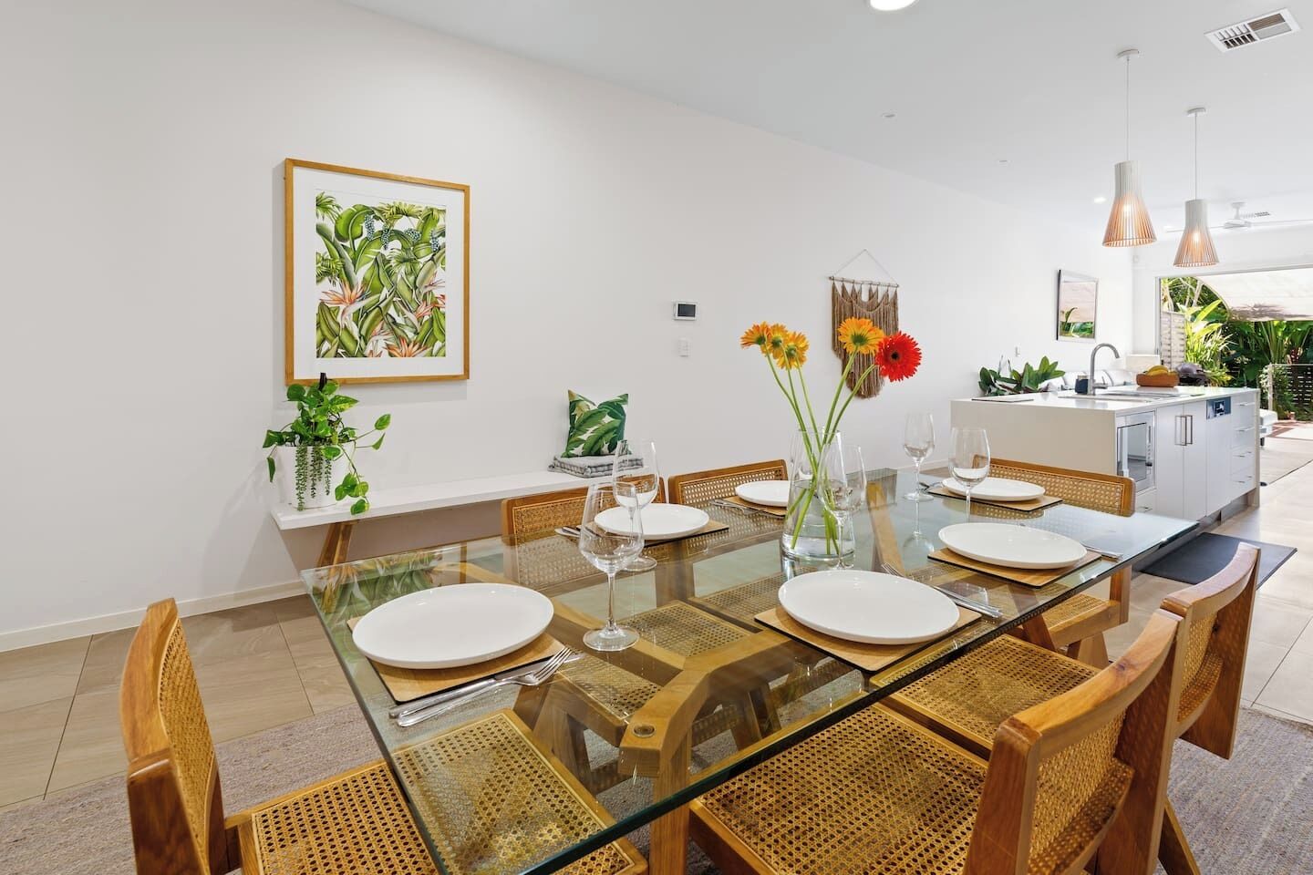 Un espace repas moderne avec une table en verre, des chaises en bois et une cuisine en arrière-plan.