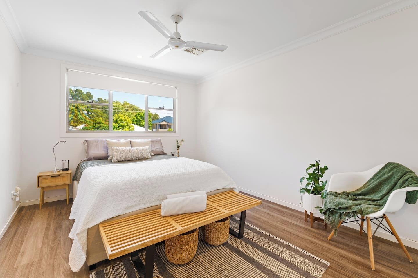 Une chambre à coucher comprenant un lit, une table de chevet, une commode, un ventilateur de plafond, une fenêtre avec vue, un banc, une chaise et une plante en pot.