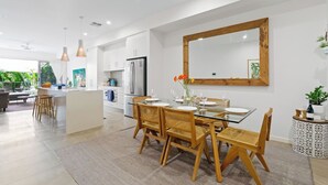 Una cocina moderna con armarios blancos, una isla grande y un comedor con mesa de vidrio y sillas de madera.