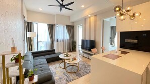 A modern living room with a sofa, a coffee table, a TV, and a kitchen area with a counter and a ceiling fan.