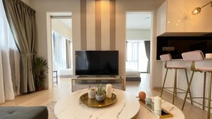 A modern living room with a flat-screen TV, two round tables, a sofa, and a kitchen area with bar stools.