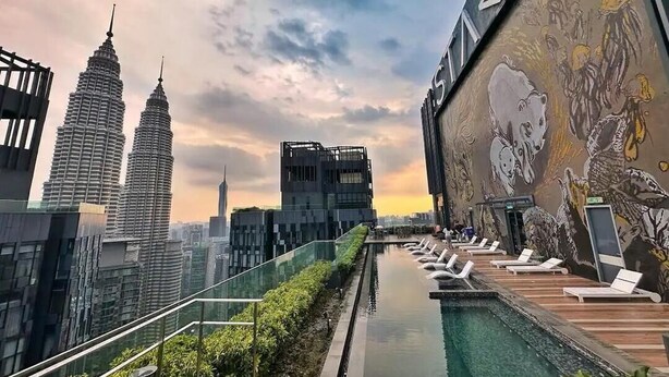 A rooftop pool with lounge chairs, a glass railing, and a mural.