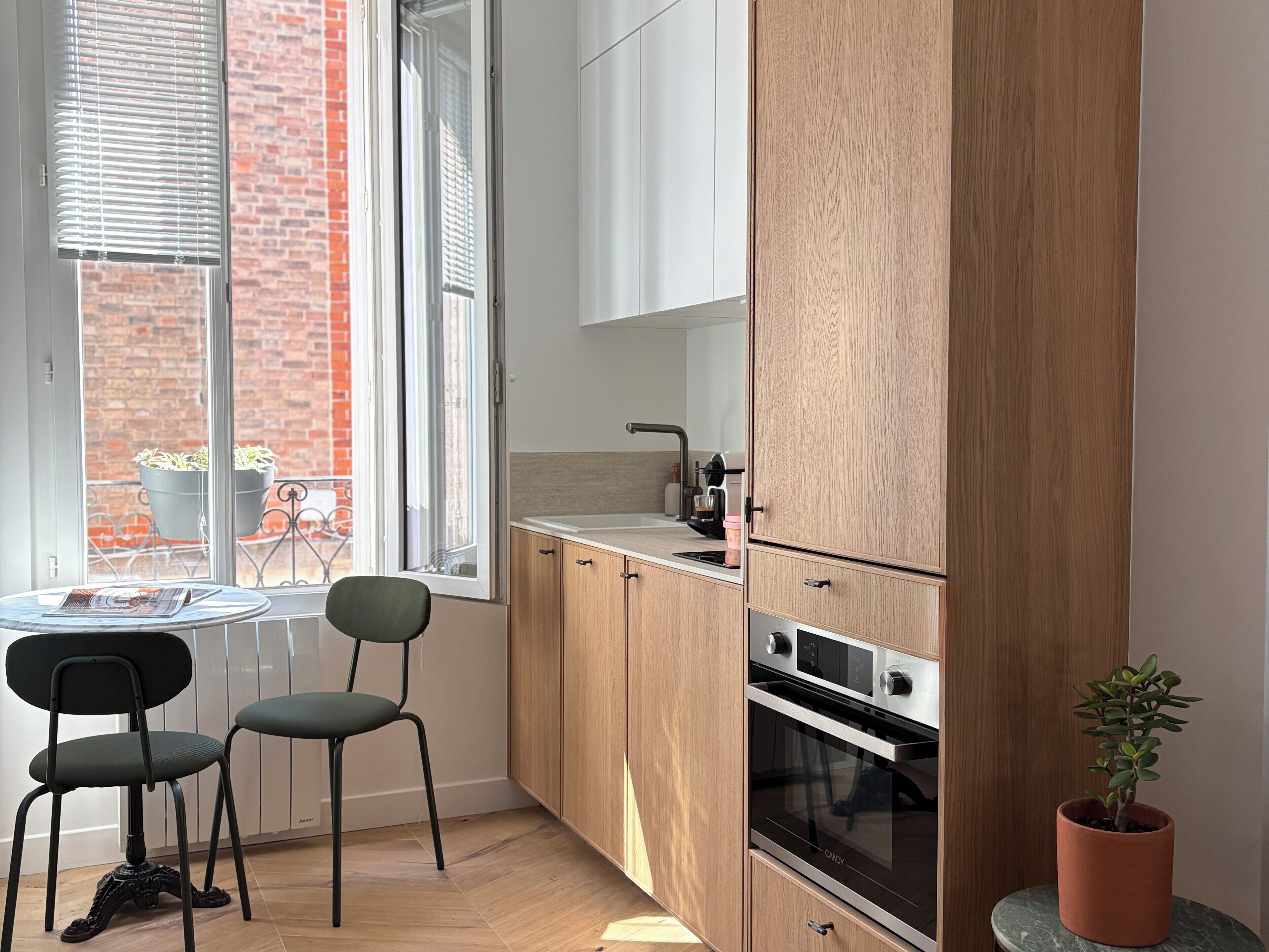 A compact kitchen with wooden cabinets, a built-in oven, and a window with blinds.