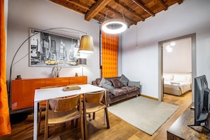 A modern living room with a dining area, a sofa, and a television.