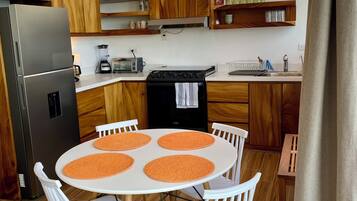Une cuisine moderne avec des meubles en bois, un réfrigérateur en acier inoxydable, une cuisinière et un coin repas comprenant une table blanche et des sets de table orange.