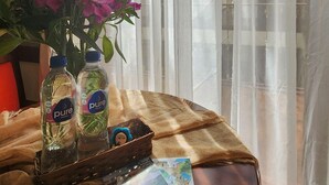 Una mesa con un florero de flores moradas, dos botellas de agua, una cesta y un folleto.