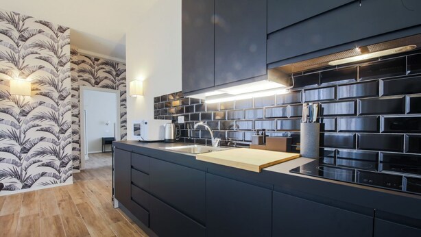 Une cuisine moderne avec des meubles de couleur sombre, un îlot central doté d’un évier et un pare-feu avec un motif géométrique.