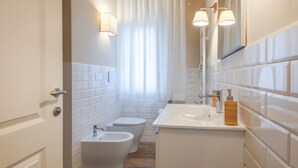 Une salle de bain avec un mur recouvert de carreaux blancs, un lavabo, un bidet et des toilettes.