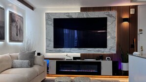 Un salon moderne doté d’un grand téléviseur à écran plat fixé sur un mur en marbre, d’un canapé et d’un petit meuble de rangement en dessous.