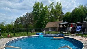 Een zwembad met een hottub in het midden, omgeven door een betegeld zonnedek en een zwarte hek.