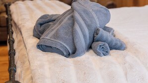Een bed met een witte, pluizige deken en opgerolde blauwe handdoeken. Achter het bed hangt een lijst met de Amerikaanse vlag.