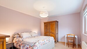 A bedroom with a bed, a wooden wardrobe, a desk, and a chair.