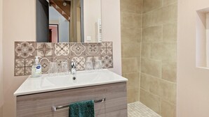 A bathroom with a white sink, a mirror, and a shower area with beige tiles.