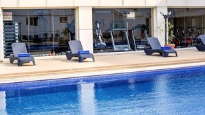 A swimming pool with lounge chairs and exercise equipment in the background. - Ah Hotel and Conferences (Accra)