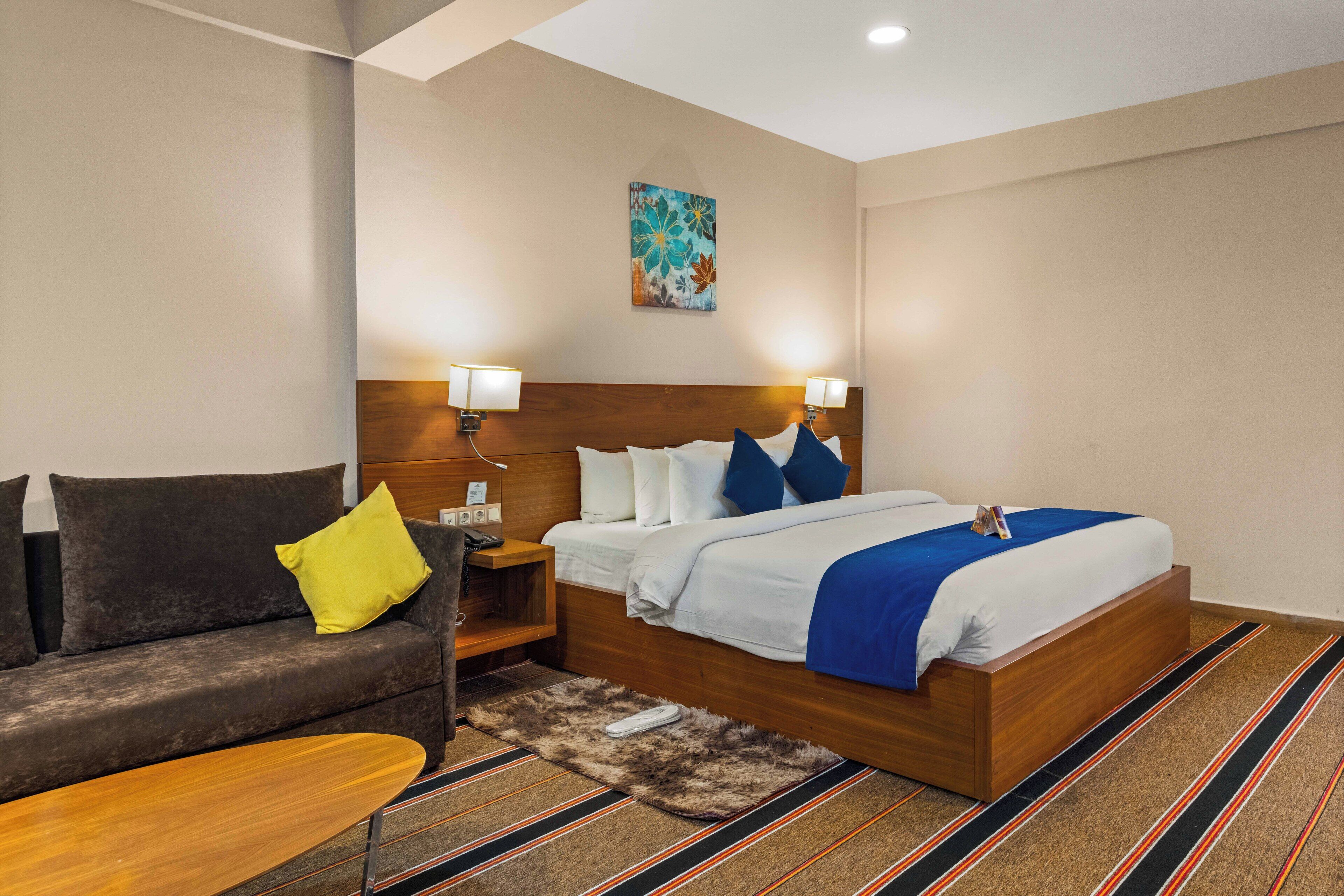 Une chambre d’hôtel avec un lit, un canapé, une table de chevet et un tableau au mur.