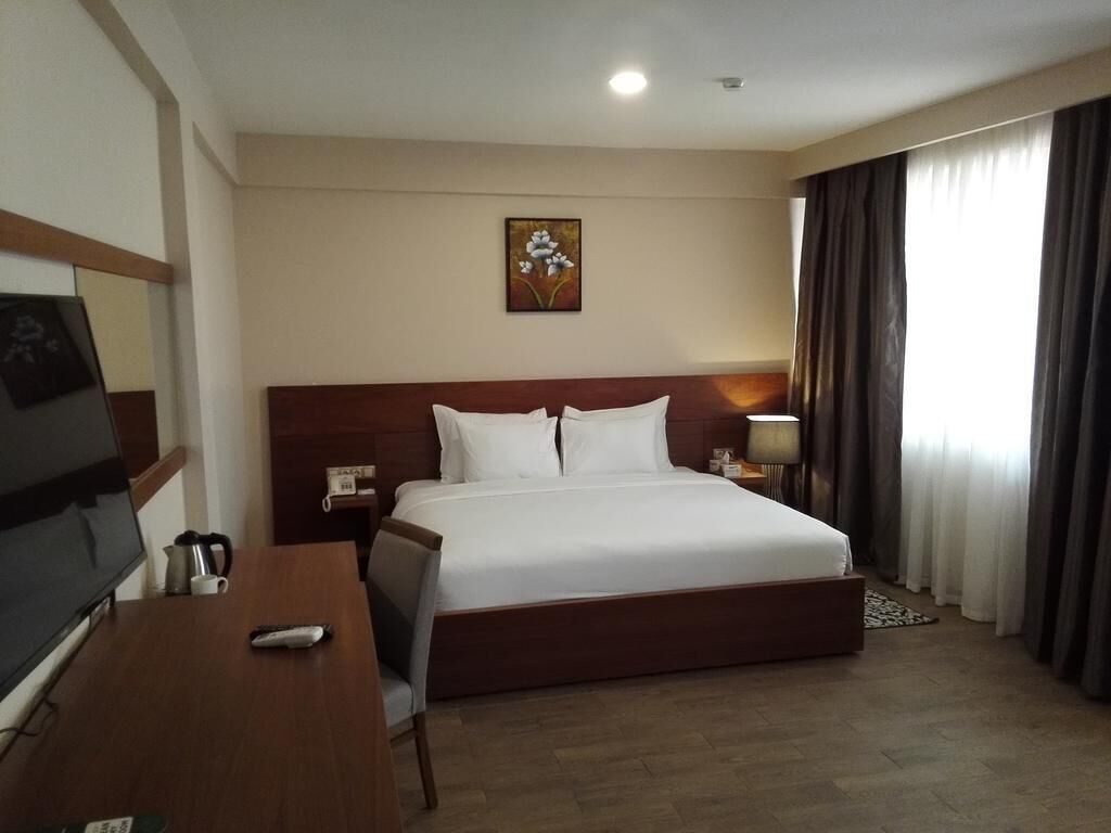 A hotel room with a bed, a desk with a TV, a lamp, and a painting on the wall.