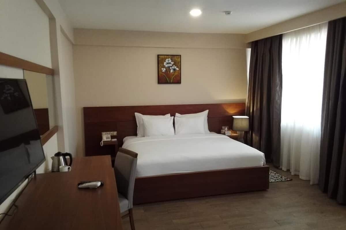 A hotel room with a bed, a desk with a TV, a lamp, and a painting on the wall.