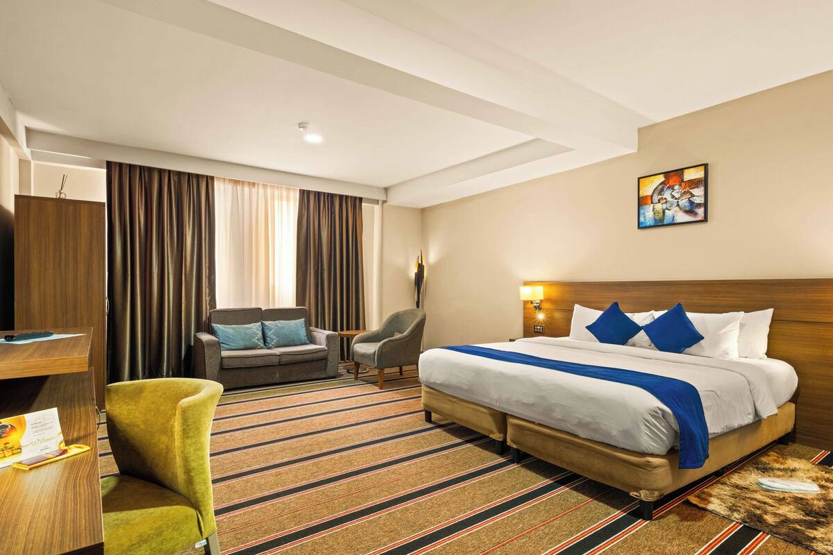 A hotel room with a large bed, two armchairs, a desk, and a large window with curtains.