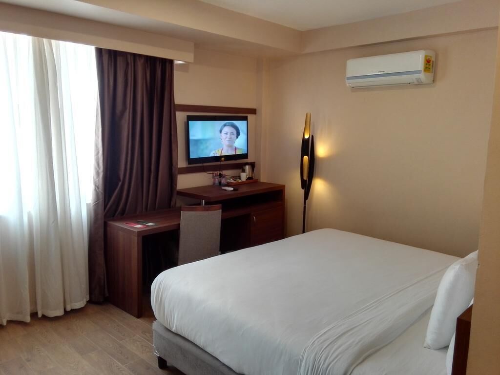 A hotel room with a bed, a desk, a television, and an air conditioning unit.
