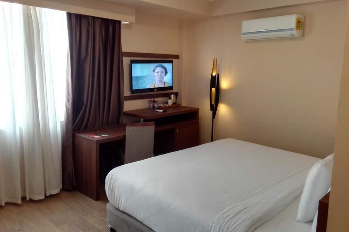 A hotel room with a bed, a desk, a television, and an air conditioning unit.